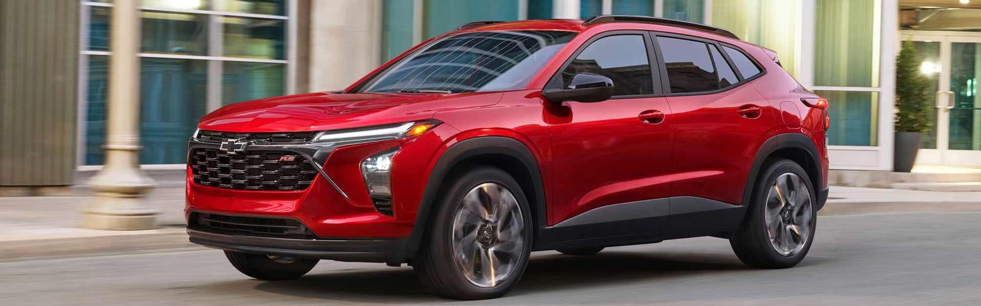 2026 Chevrolet Trax in red, parked on a city street near modern buildings.